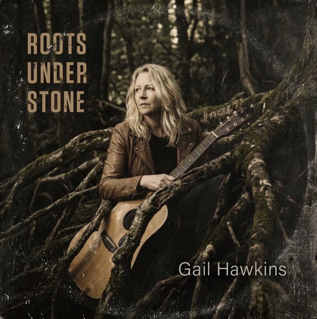 The album cover for the song Roots Under Stone by Gail Hawkins in which a blond woman holds an acoustic guitar in a dark forest.